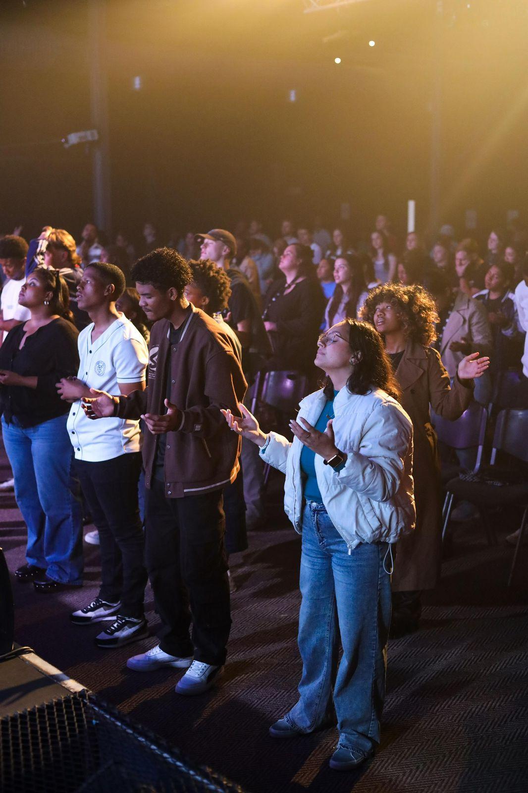 A crowd worshipping together with hands raised at First Thursday